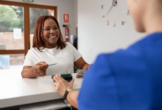Smiling woman handing payment card to dental receptionist