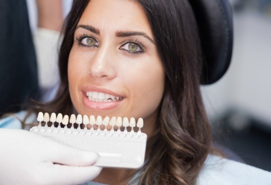 Woman smiling with row of dental veneers held by cosmetic dentist in Farmington Hills