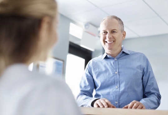 Man in blue collared shirt smiling at dental receptionist