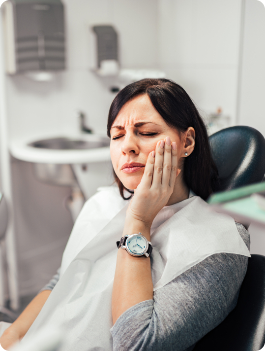 Woman in dental chair holding side of her face in pain