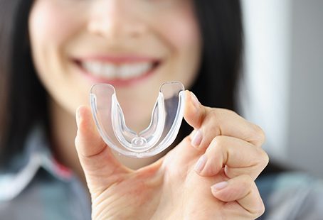 Closeup of smiling woman holding clear mouthguard