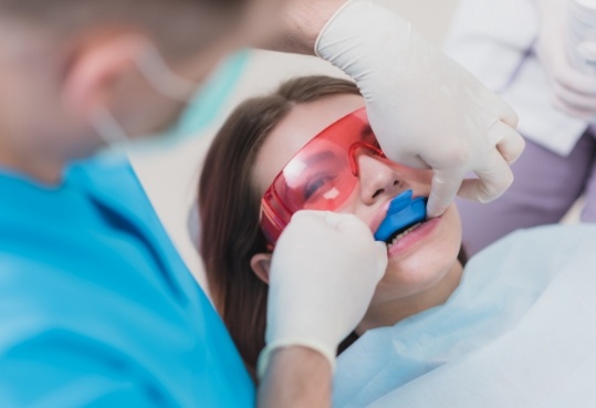 Dentist placing tray over teeth of young woman in dental chair
