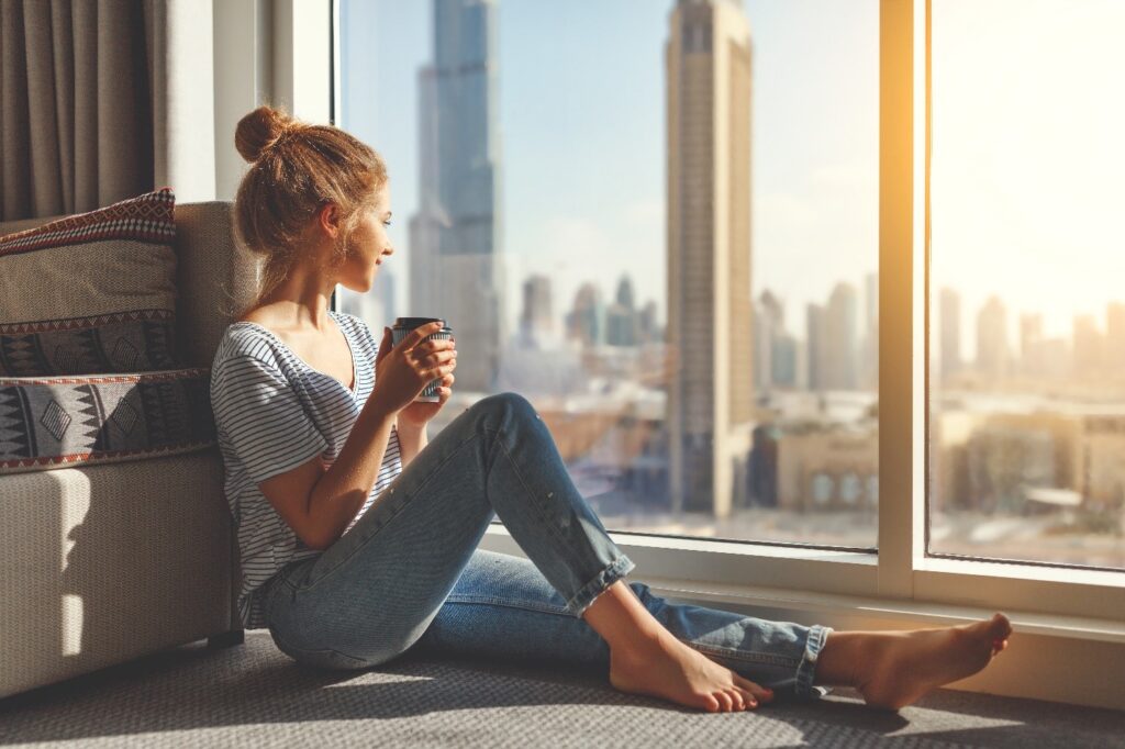 Woman smiling while looking out of hotel window and drinking tea
