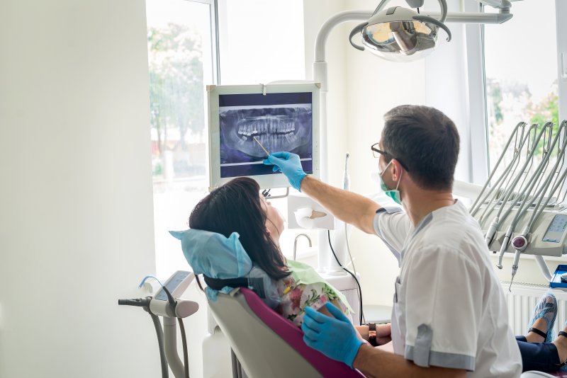 A dentist pointing at a patient’s dental X-rays