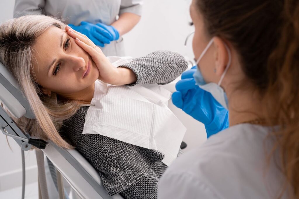 A woman sitting in a dental chair holding her jaw in pain.